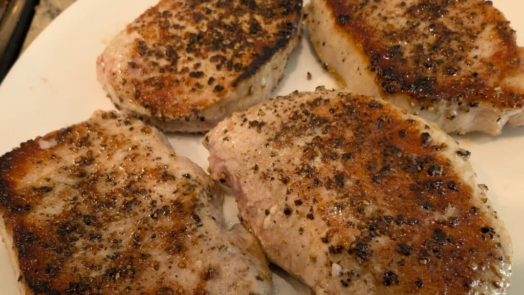 Juicy grilled pork chops seasoned with black pepper and herbs, cooked to perfection, served on a white plate, showcasing a delicious and savory meal.