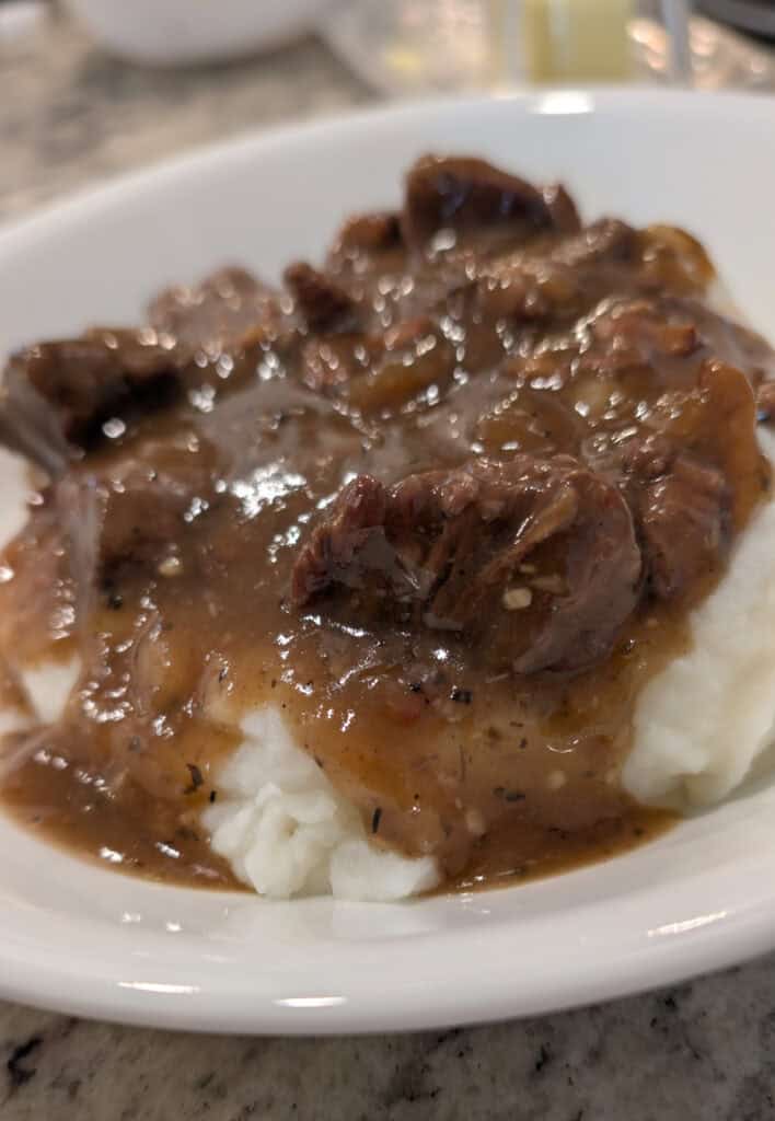 Succulent beef stew served over creamy mashed potatoes in a white bowl, hearty comfort food with tender meat and rich gravy for a satisfying meal.