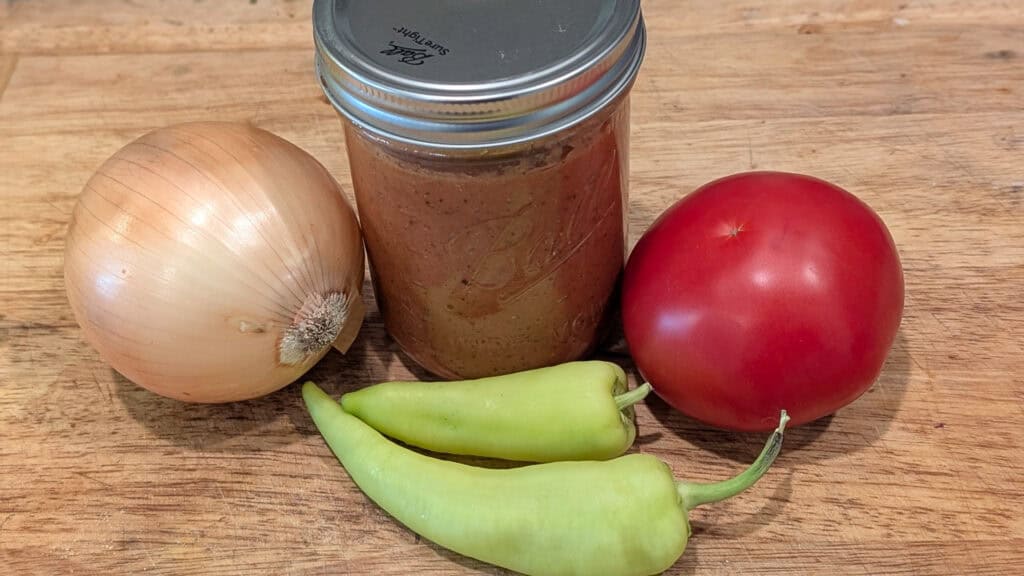 Creamy homemade tomato soup with fresh onion, green peppers, and a ripe tomato on a wooden surface. Perfect for a comforting and flavorful meal, showcasing fresh ingredients for a delicious dish.
