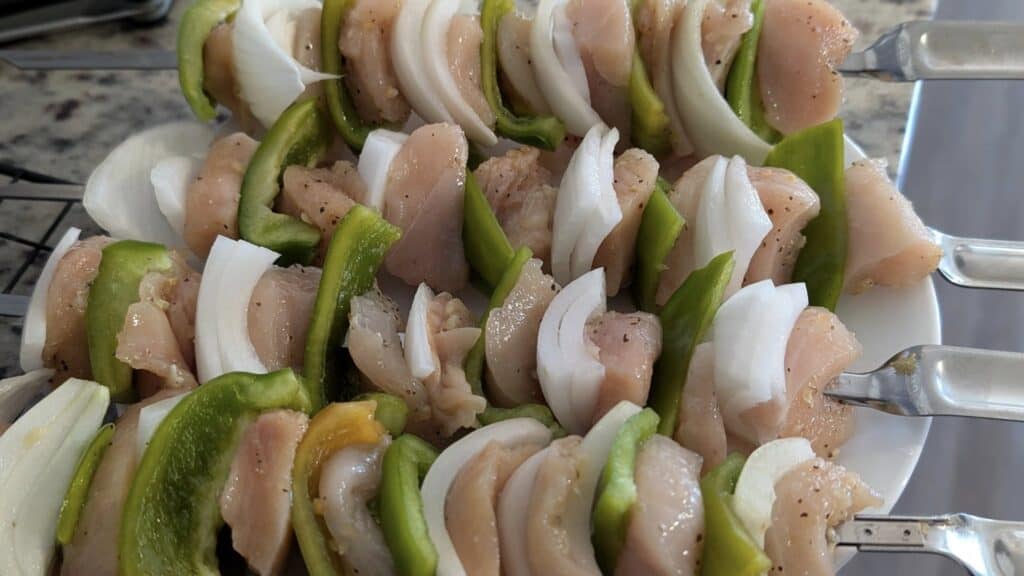 Skewers with raw chicken, green bell peppers, and onions ready for grilling, highlighting fresh ingredients and delicious barbecue prep.