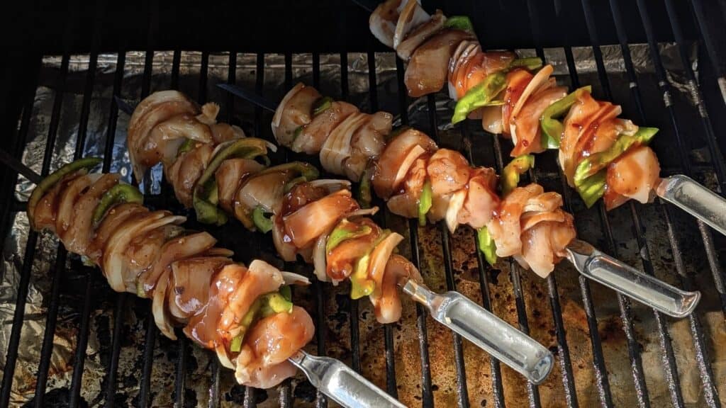 Juicy chicken and vegetable skewers grilling on barbecue grill, perfect for outdoor cooking and BBQ parties, featuring marinated chicken, bell peppers, and onions.