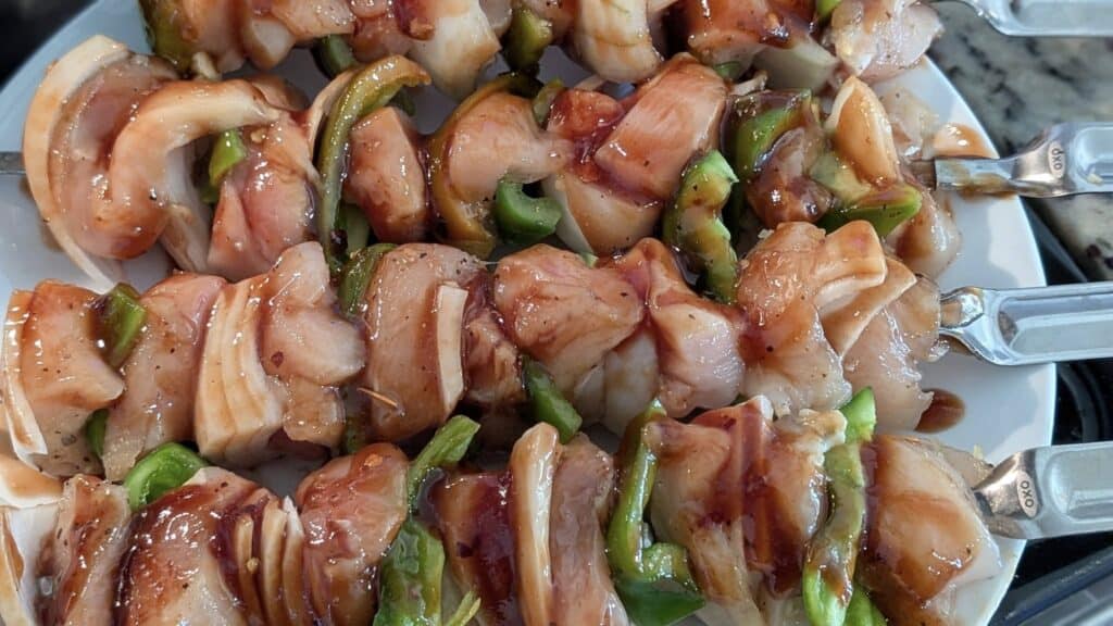 Grilled chicken and vegetable skewers with chicken, green peppers, and onions coated in a savory glaze on a white platter.