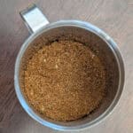 Ground spice blend in clear jar with silver lid, close-up, top view of seasoning mixture, perfect for enhancing flavor in cooking or baking, on a wooden surface.