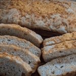 Crispy garlic bread slices on wooden serving board, toasted bread with crispy crust, homemade garlic bread, artisanal bread loaf, golden-brown toasted bread slices.