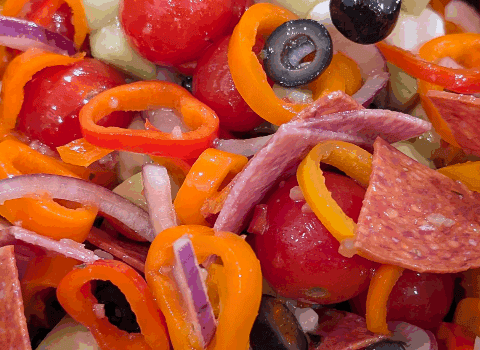 Colorful vegetable salad with cherry tomatoes, red onions, bell peppers, black olives, cucumbers, and pepperoni slices, vibrant and fresh, perfect for healthy snacking or meal prep.