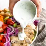 Creamy herb dressing being poured over grilled chicken and fresh vegetable salad for a light, flavorful meal. Perfect for summer lunch or healthy dinner options.
