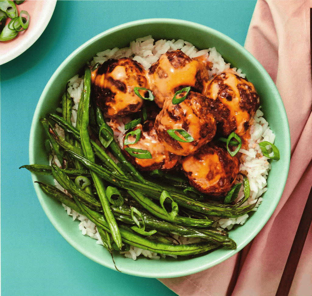 Succulent meatball bowl with rice and green beans, healthy meal with flavorful sauce, vibrant food image for comfort food and dinner ideas, served in a pastel green bowl.